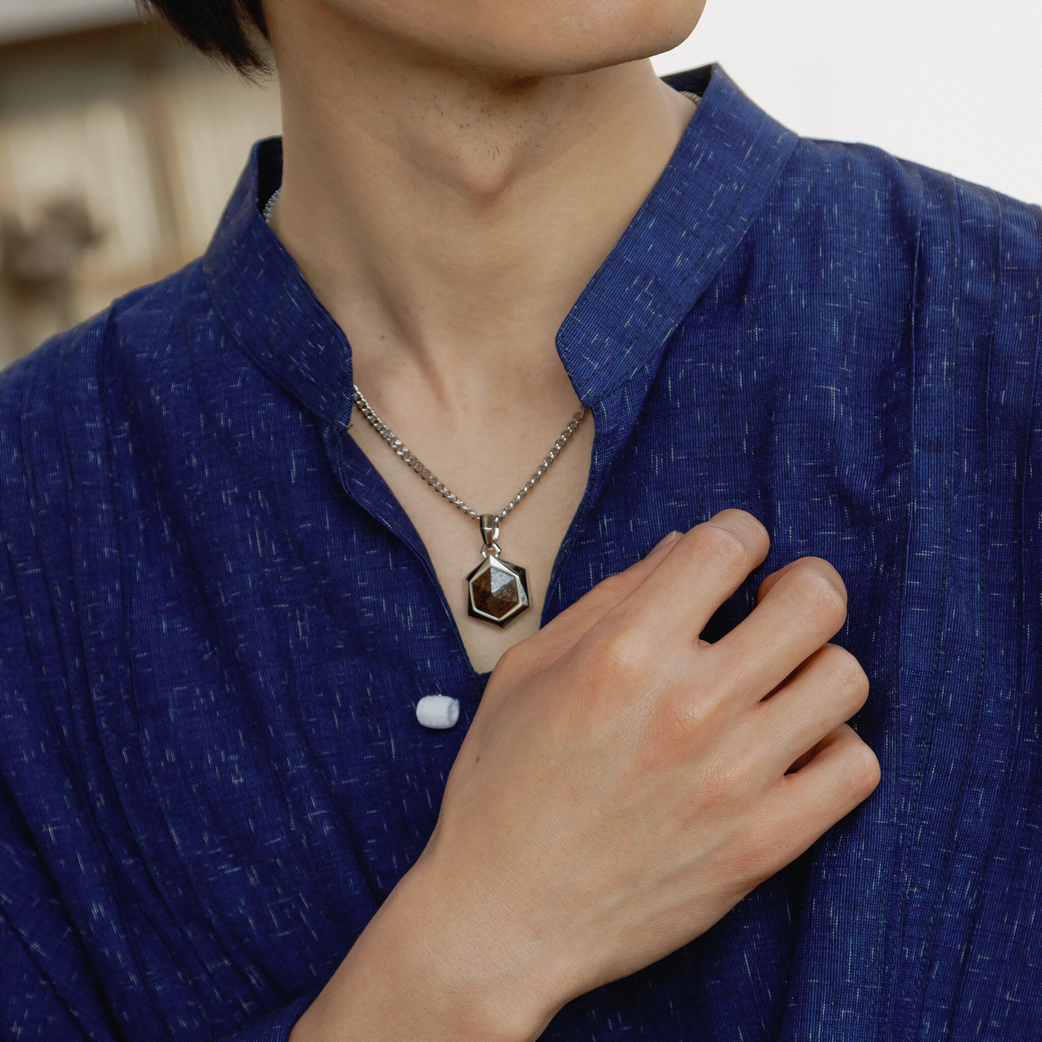 青いシャツを着ている男性の首元にAWNLの古銅輝石六角ネックレスをつけている