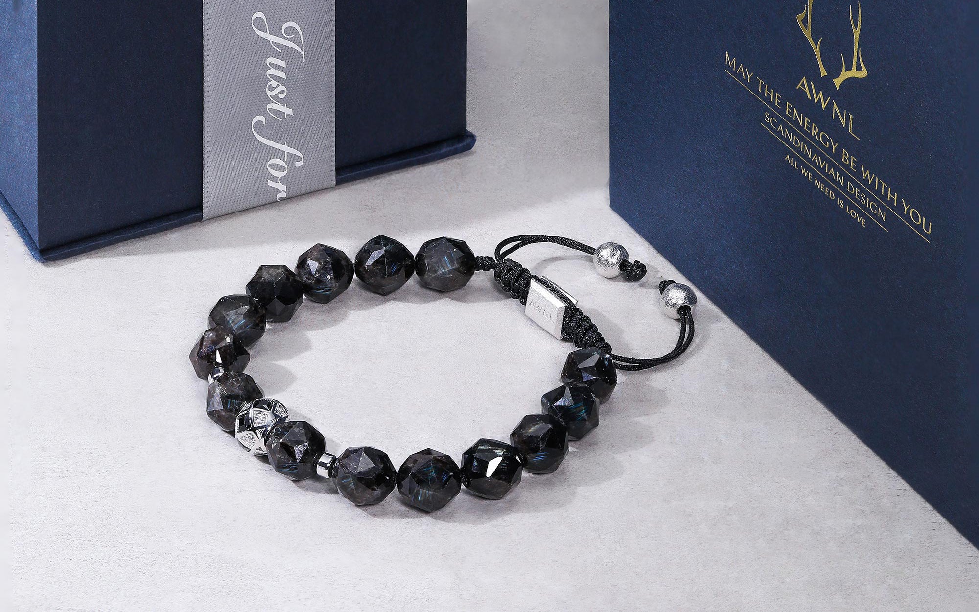 2つのAWNLの青いケースに囲まれた黒い編み紐ヌーマイトブレスレット